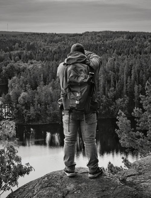 Free A photographer stands on a cliff capturing a vast forest and lake view, embodying adventure and nature photography. Stock Photo