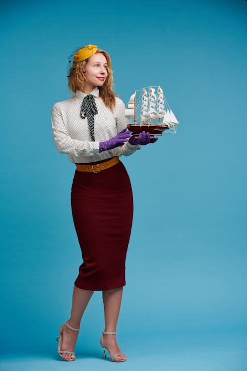 Woman in a Retro Outfit Holding a Model of a Sailing Ship