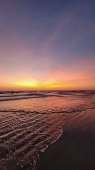 A tranquil beach at sunset with vibrant colors illuminating the sky and reflecting on the ocean.