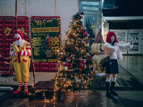 Young Woman Taking Selfie with Christmas Tree on Sidewalk Next to McDonalds Clown