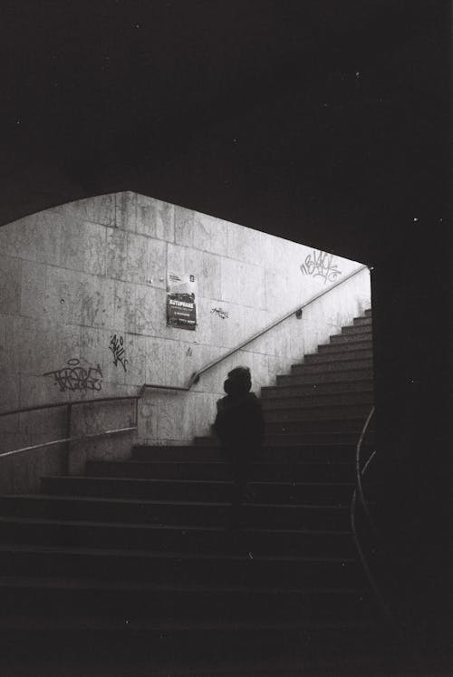 Black and White Photo of a Person Walking Up the Stairs from a Tunnel 