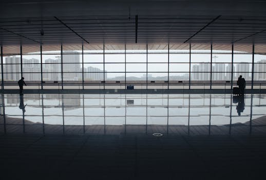 Spacious airport terminal with floor reflections, large windows, and city skyline view.