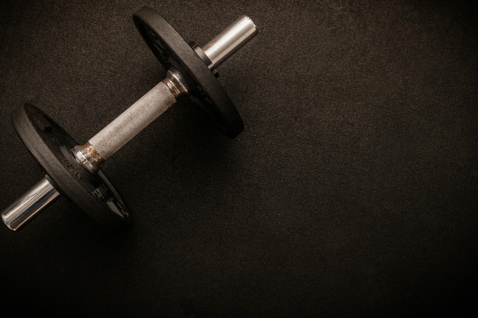 Loadable dumbbell on the floor at the gym. Top down view flat lay with bodybuilding equipment on a black background and empty space for text. Fitness, weight training or healthy lifestyle ...