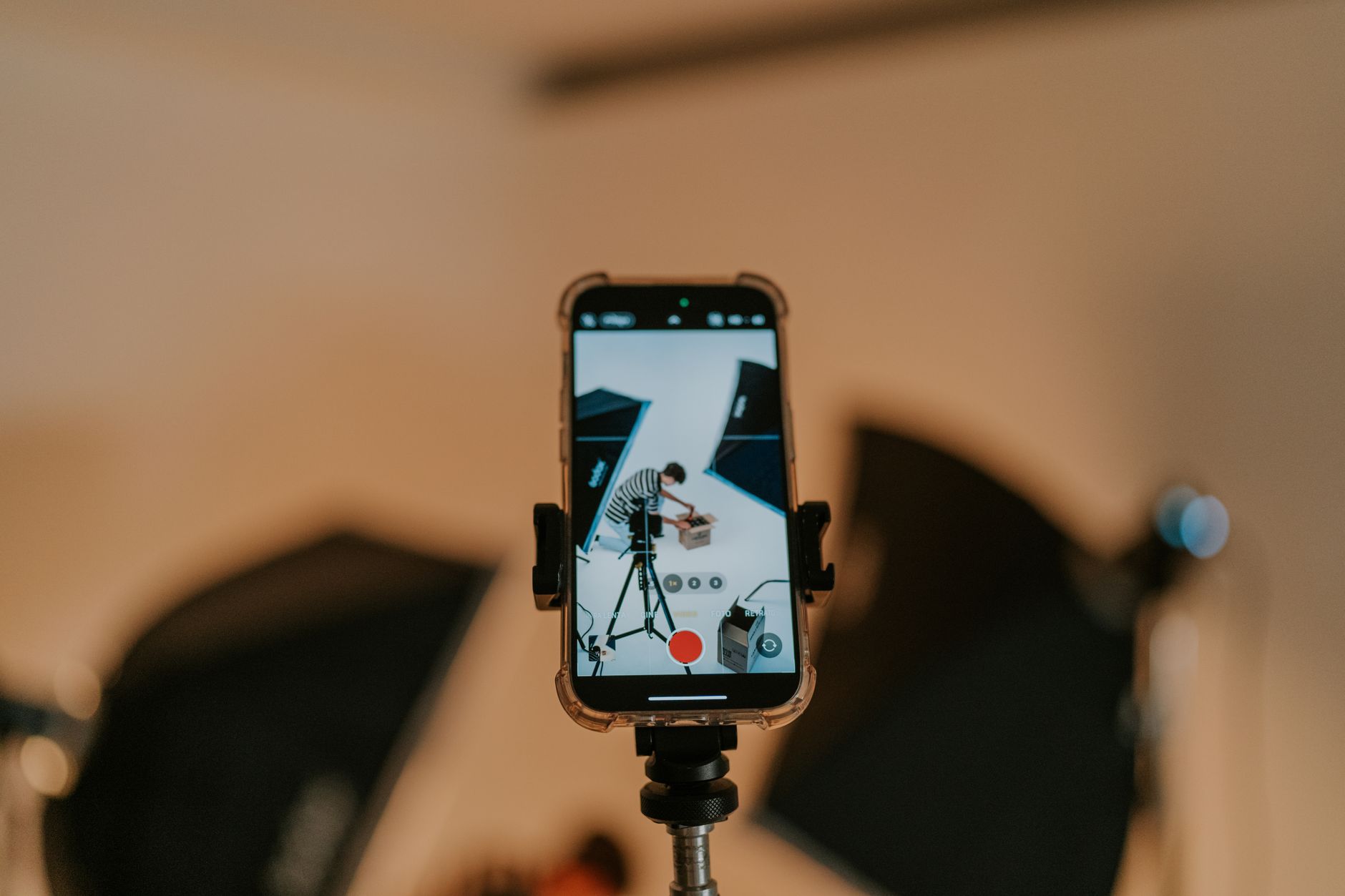 手機產品拍攝指南:小型棚架、補光燈與反光板實用技巧 Close-up of a smartphone on a tripod capturing a photo shoot in a studio setting.