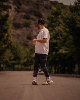 Casual man in white t-shirt and trainers standing on a scenic mountain road.
