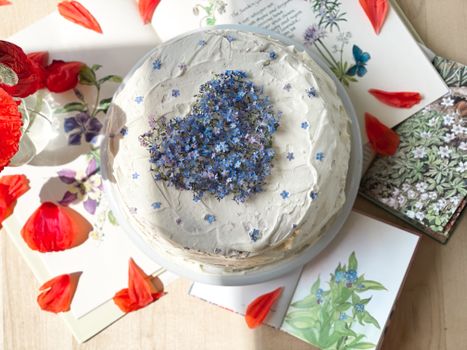 A beautifully decorated cake with blue flowers surrounded by books and red petals in Norway.
