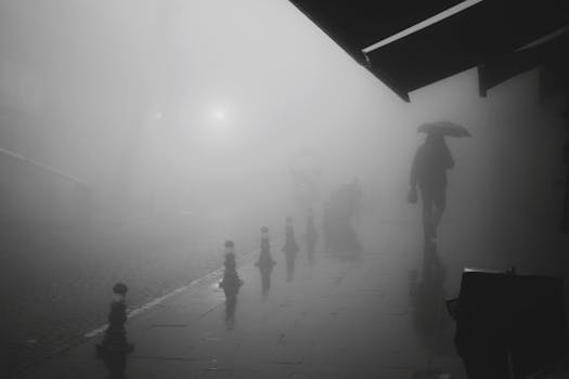 Silhouetted person with umbrella on a foggy city street, creating a mysterious and atmospheric scene.