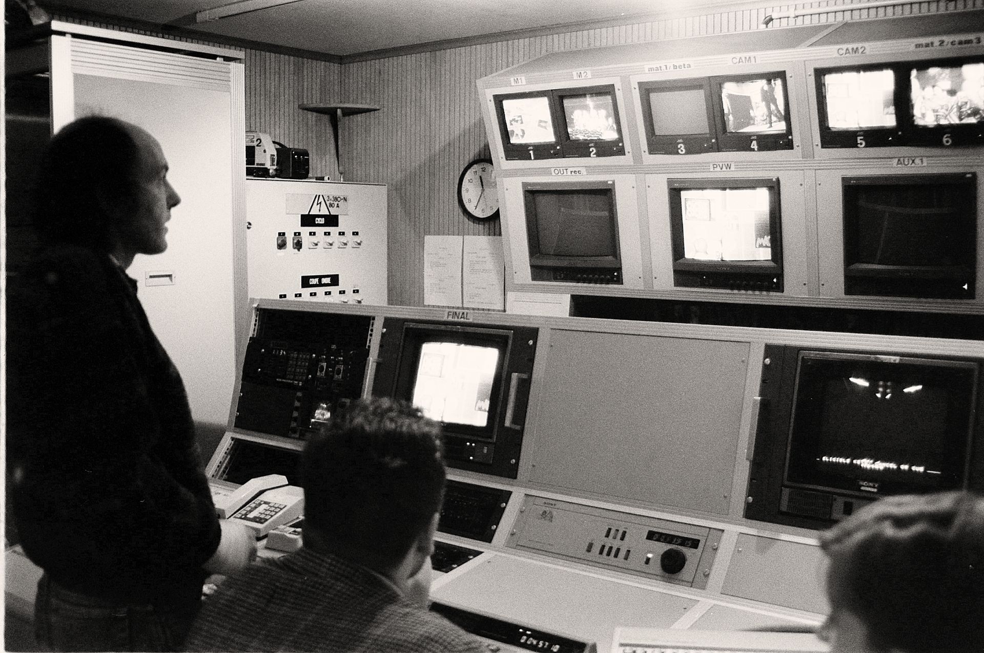 Men working in a vintage broadcasting control room filled with analogue equipment and monitors.