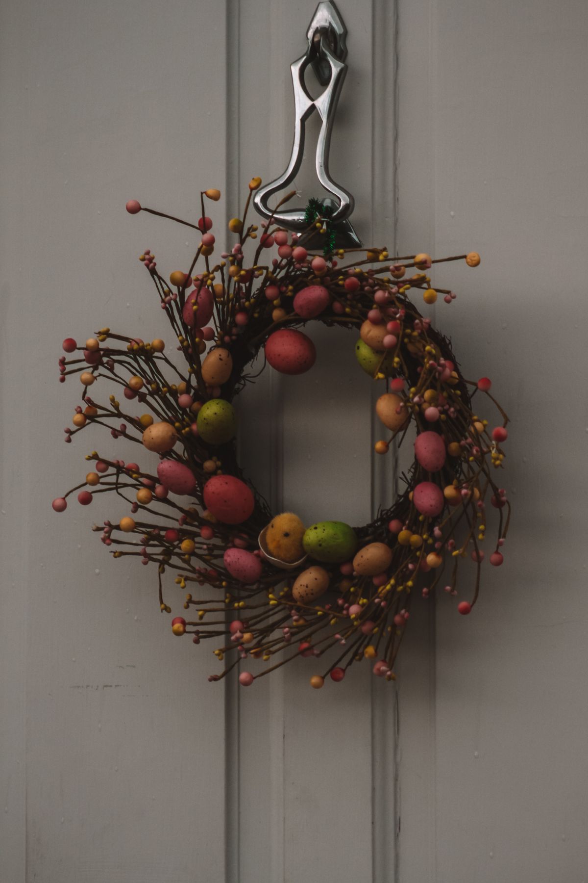 A vibrant Easter wreath adorned with colorful eggs and twigs, hanging on a classic door. Stock Photo.