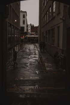 Capture of a tram in a moody urban alley during rain, with reflections on wet pavement.