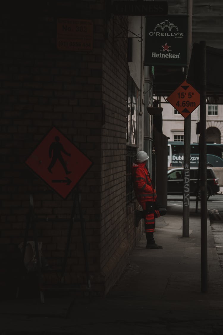 Construction Worker In Orange High Visibility Clothing And White Hardhat Standing On A Street