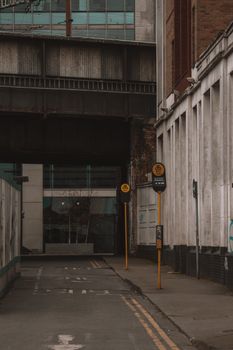 Moody urban alley showcasing industrial architecture and signposts under an overpass.