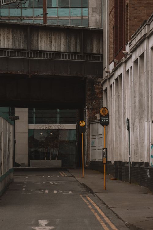 Free Moody urban alley showcasing industrial architecture and signposts under an overpass. Stock Photo