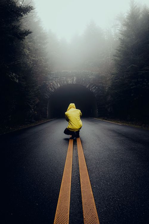Free A solitary figure in a yellow jacket approaches a dark tunnel in a foggy forest, evoking mystery and adventure. Stock Photo