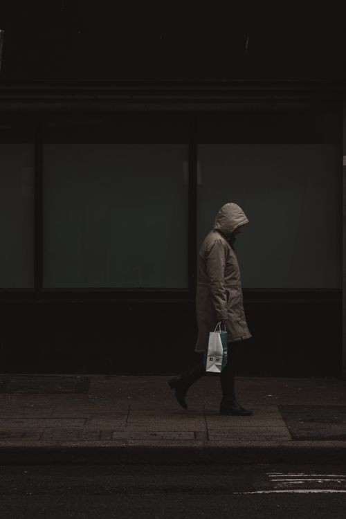 Free A person in a hooded coat walking alone on an urban sidewalk, evoking solitude. Stock Photo