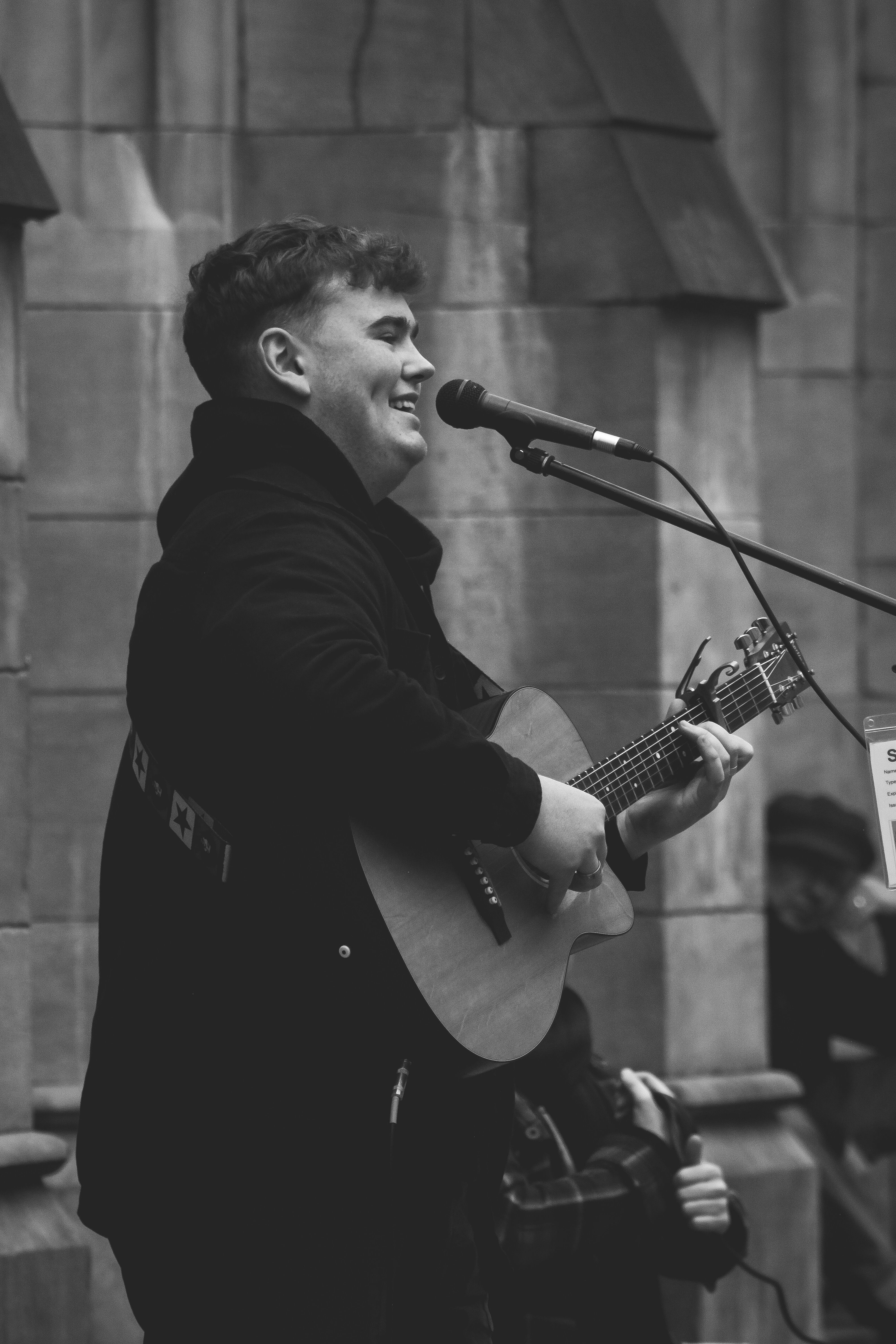 Black and white photo of a man singing and playing guitar on city streets.