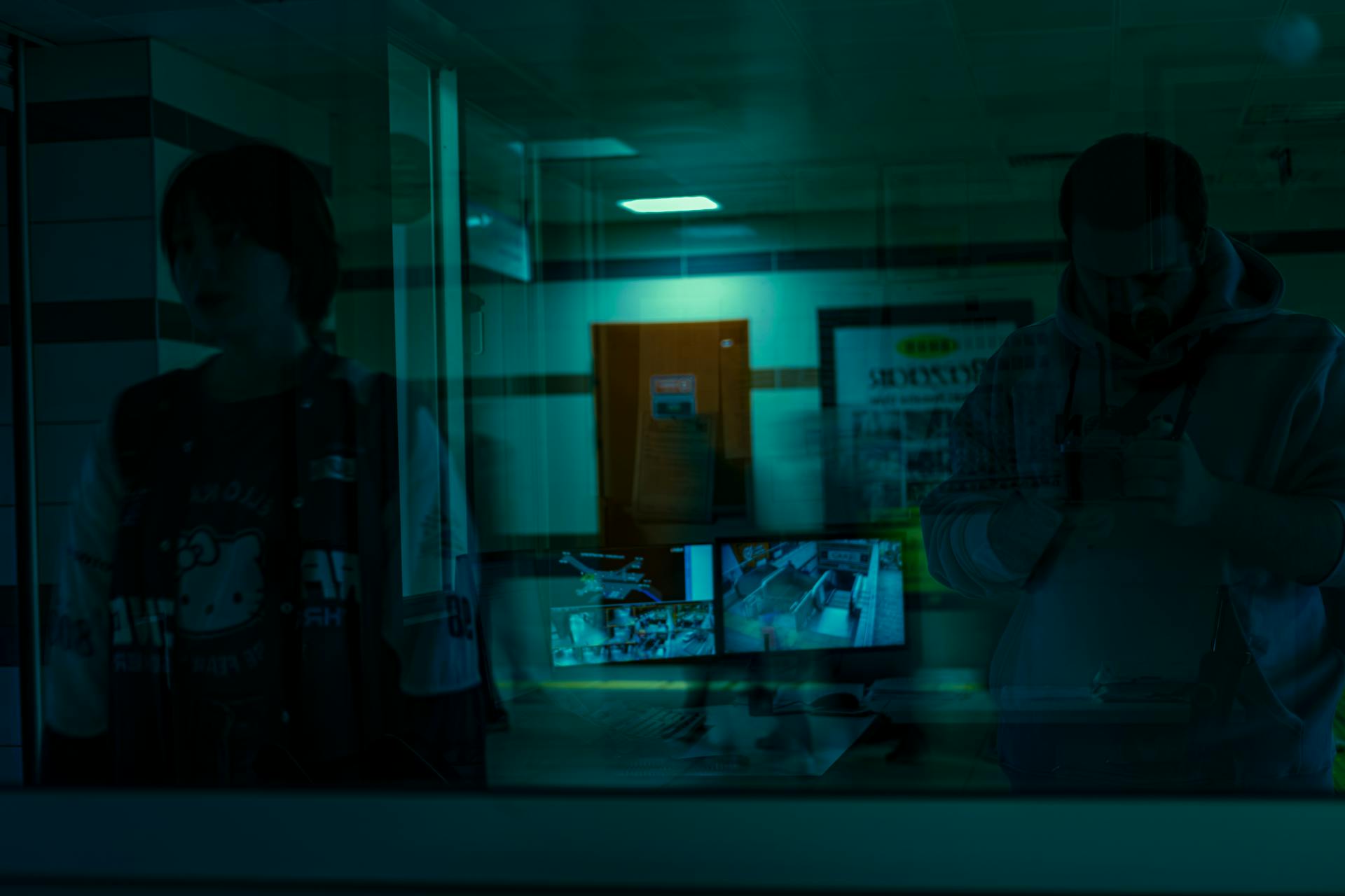 Shadowy figures reflected with security monitors in the foreground.