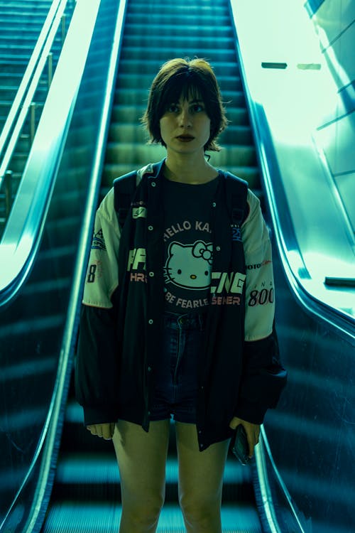 Photo of a Woman Wearing a Blouse with Graphics and a Jacket, Standing on an Escalator