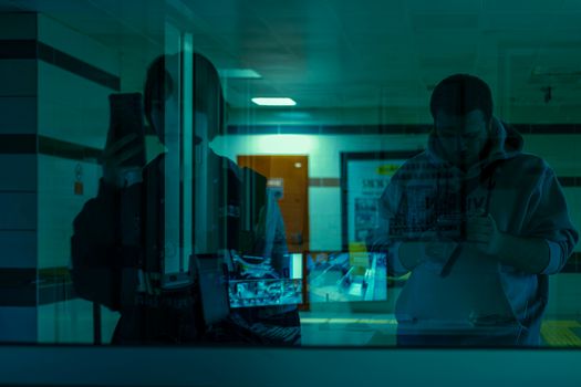 Artistic reflection of two people in a hospital corridor with blue lighting.