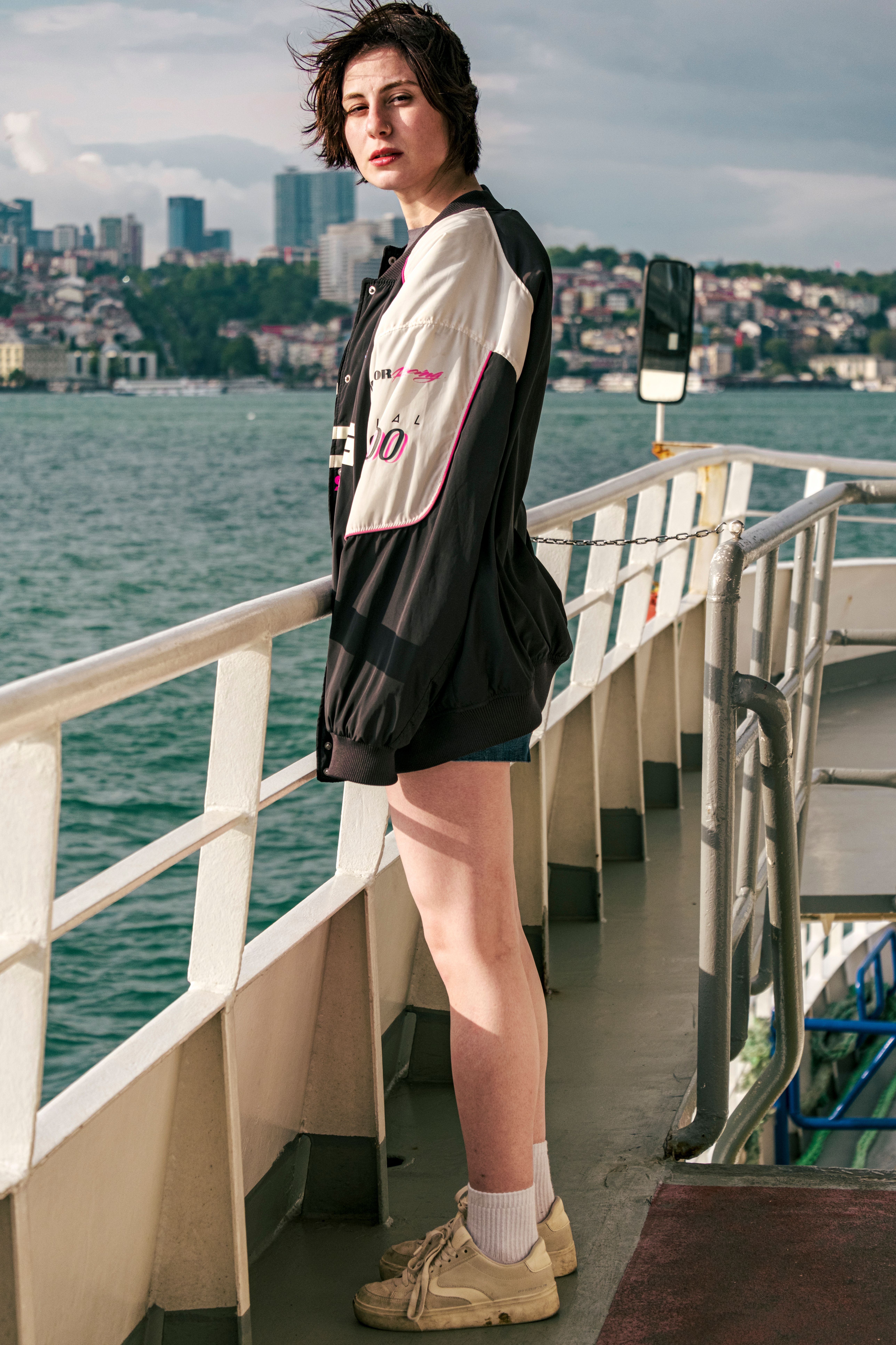 Young woman stands on a ferry deck enjoying a city waterfront view, embodying travel and exploration.