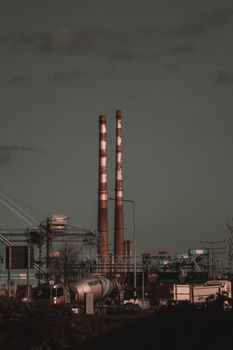 A vertical shot of an industrial factory with striped chimneys amidst a gray sky, emphasizing urban pollution.