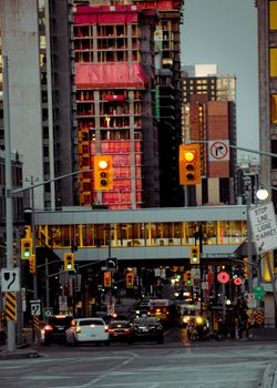 High-rise buildings loom over a bustling city street with traffic lights and cars during twilight.