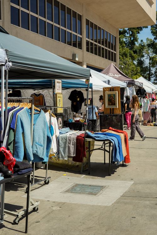 Free Busy outdoor flea market with various clothing stalls and people shopping during the day. Stock Photo