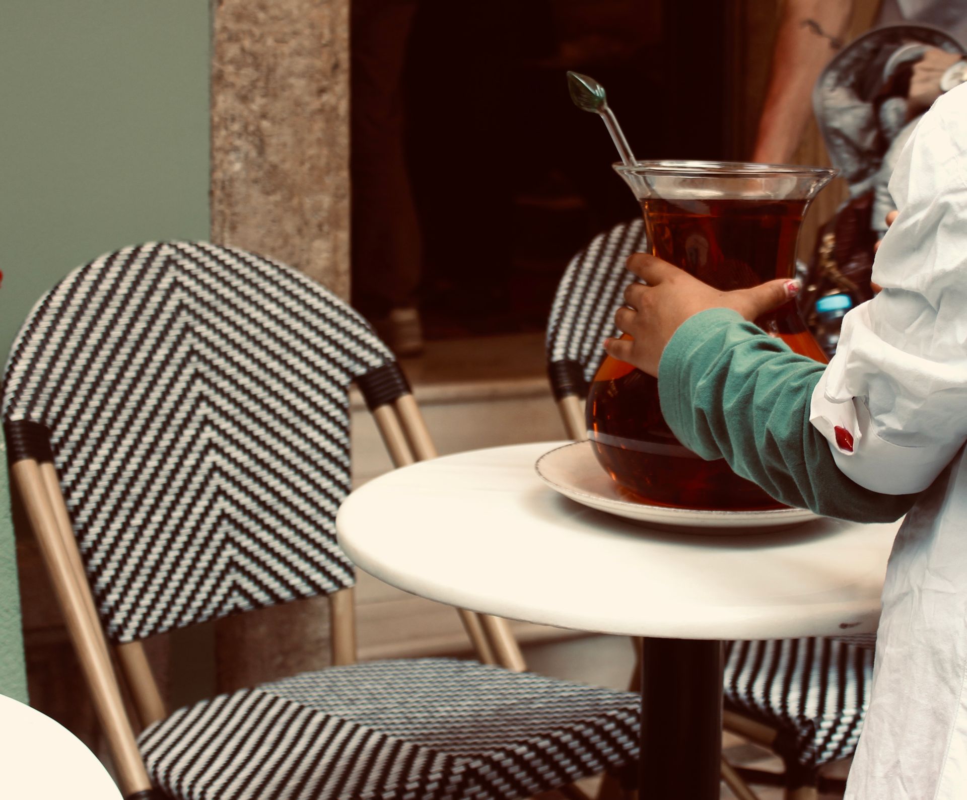 Waitress serving a jug of iced tea at an outdoor bistro with patterned chairs.