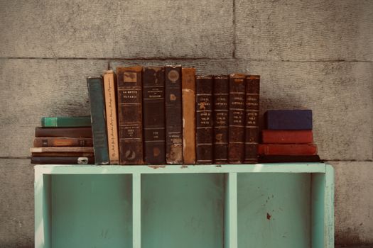 A collection of vintage books displayed on a teal shelf against a textured wall.