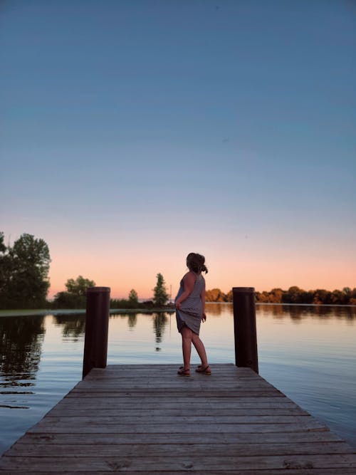 Woman in a Dress Standing on the Pier at Sunset 