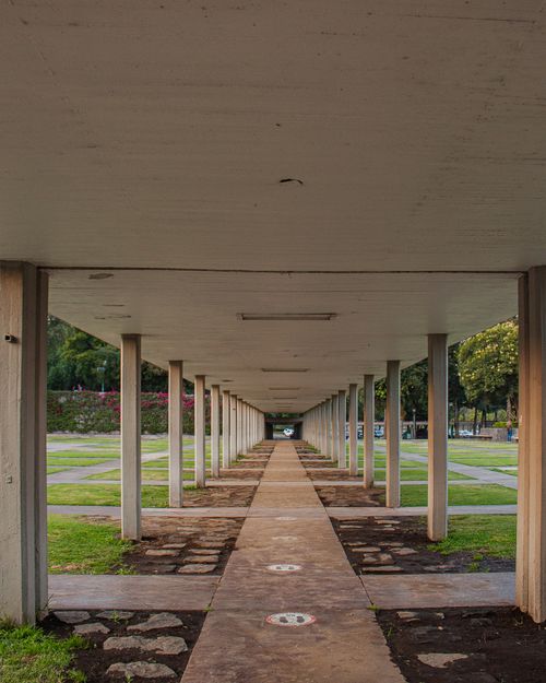 Free A symmetrical view of a modern concrete column walkway in a park setting under clear daylight conditions. Stock Photo