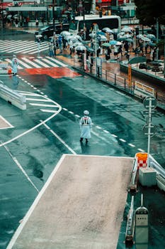 A police officer directs traffic on a rainy street in Tokyo, Japan under umbrellas.