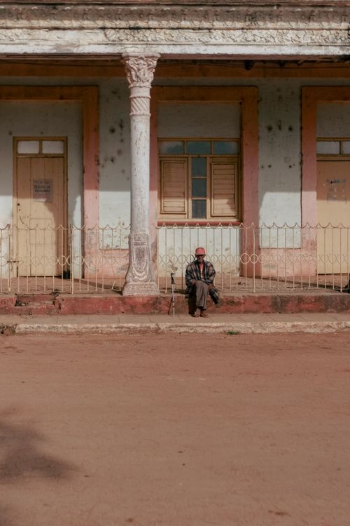 Free A man sits alone on a rustic building porch, embodying solitude and history. Stock Photo