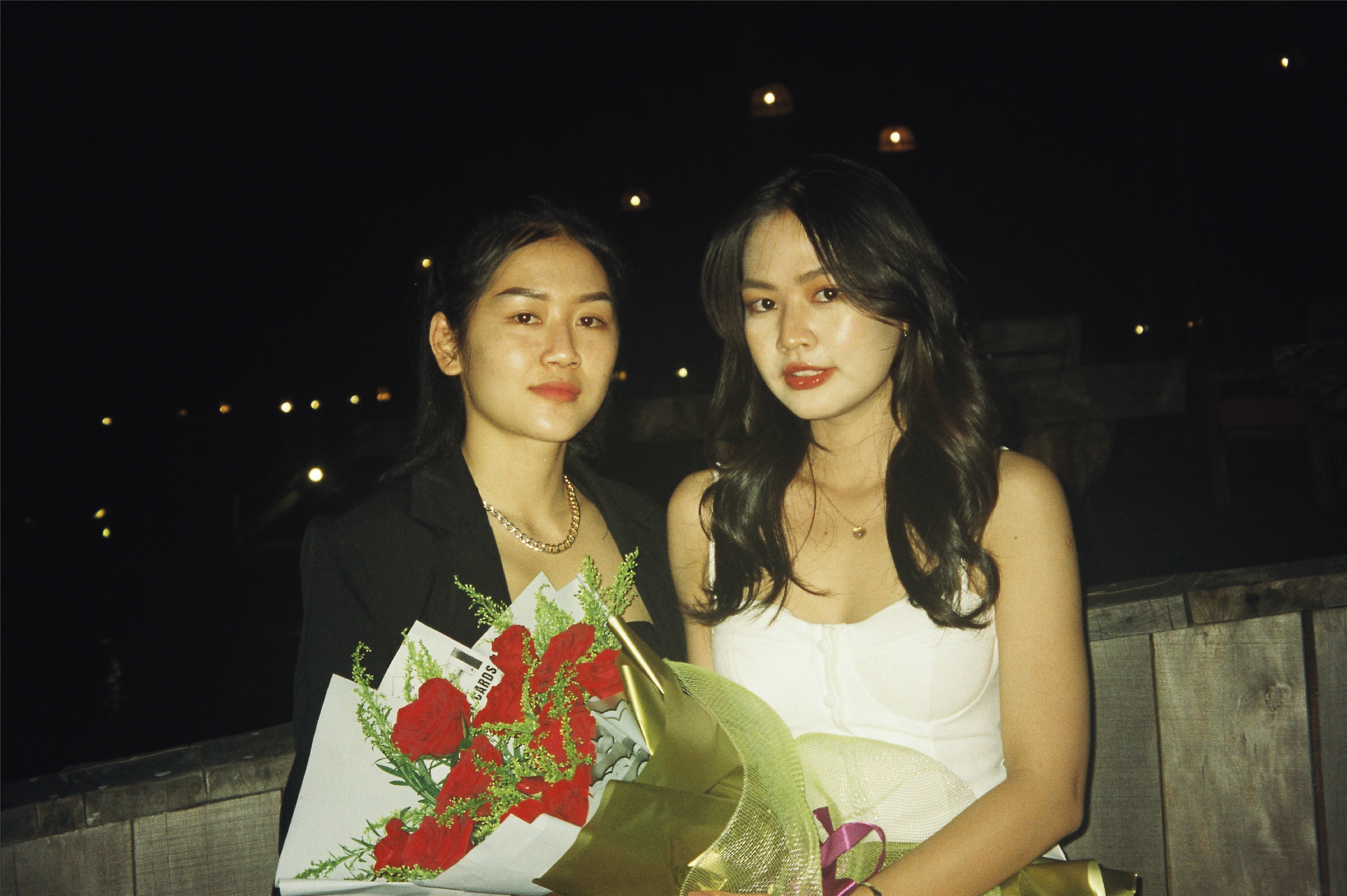 Two women with bouquets of flowers posing together at night in Phu Quoc, Vietnam.