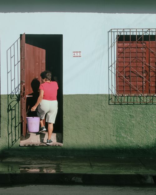 Free Adult woman entering a building carrying a purple bucket on a sunny day. Stock Photo