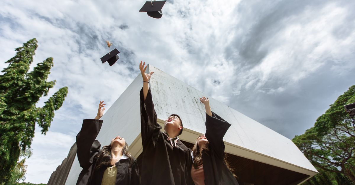 A graduation cap being tossed in the air, with a laptop showing a job portal in the background