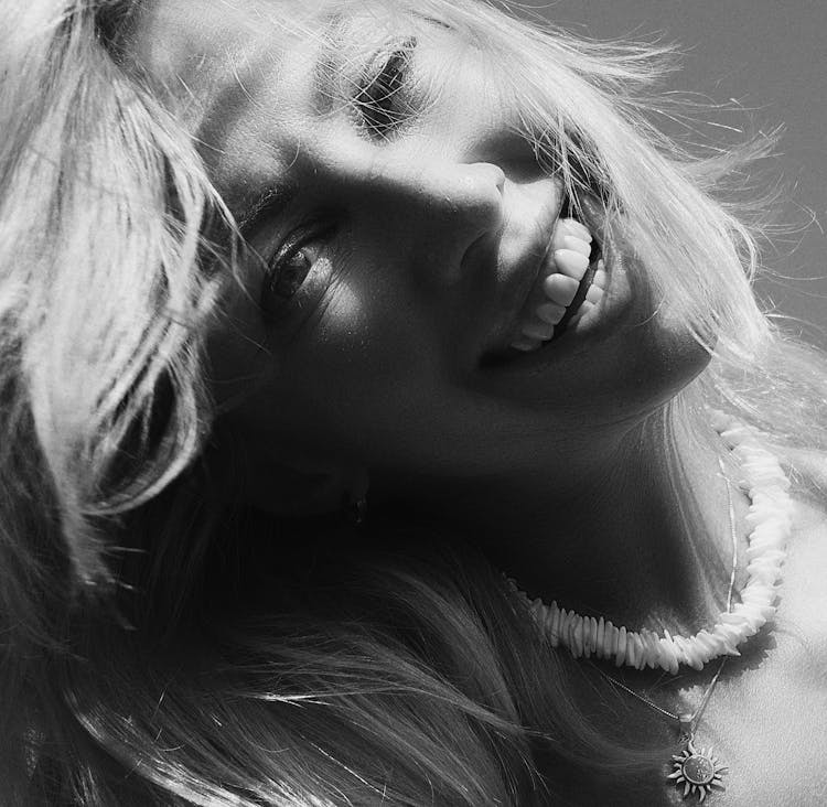 Black And White Portrait Of A Laughing Young Woman Waering A Necklace With A Sun Pendant