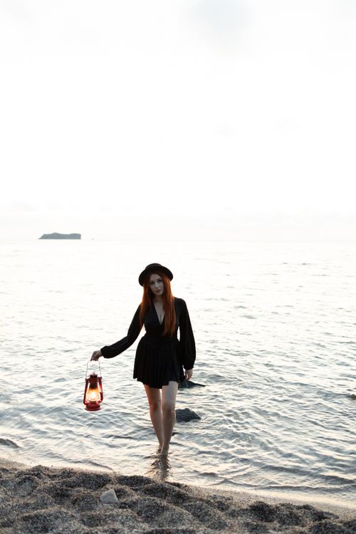 Free Serene scene of a woman with a lantern walking on a Turkish beach during sunset. Stock Photo