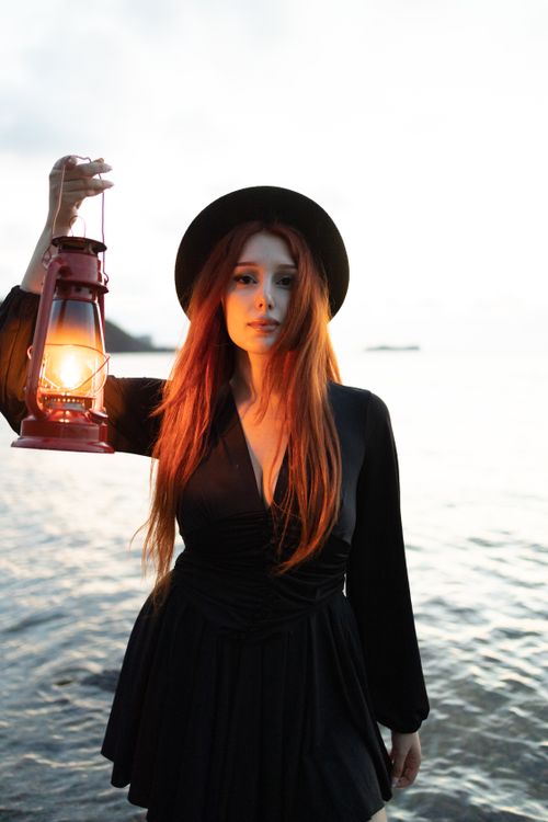 Free Young woman holding a lantern by the sea at twilight, creating a mysterious atmosphere. Stock Photo