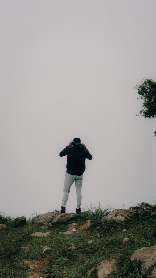 Free Man in hoodie standing on a hillside in Idukki, Kerala, surrounded by fog. Stock Photo