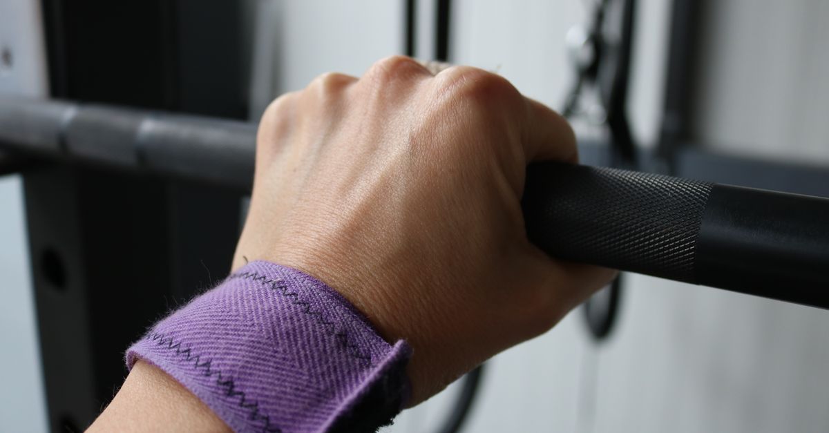 A woman's hand with a wristband gripping a barbell in a gym setting. Focus on strength and exercise.