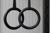 Close-up of set of black gymnastic rings or steady rings hanging in steel power rack over a white wall. Fitness or healthy lifestyle concept