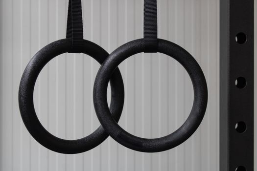 Detailed view of two black gymnastic rings hanging indoors, perfect for workout and strength training visuals.