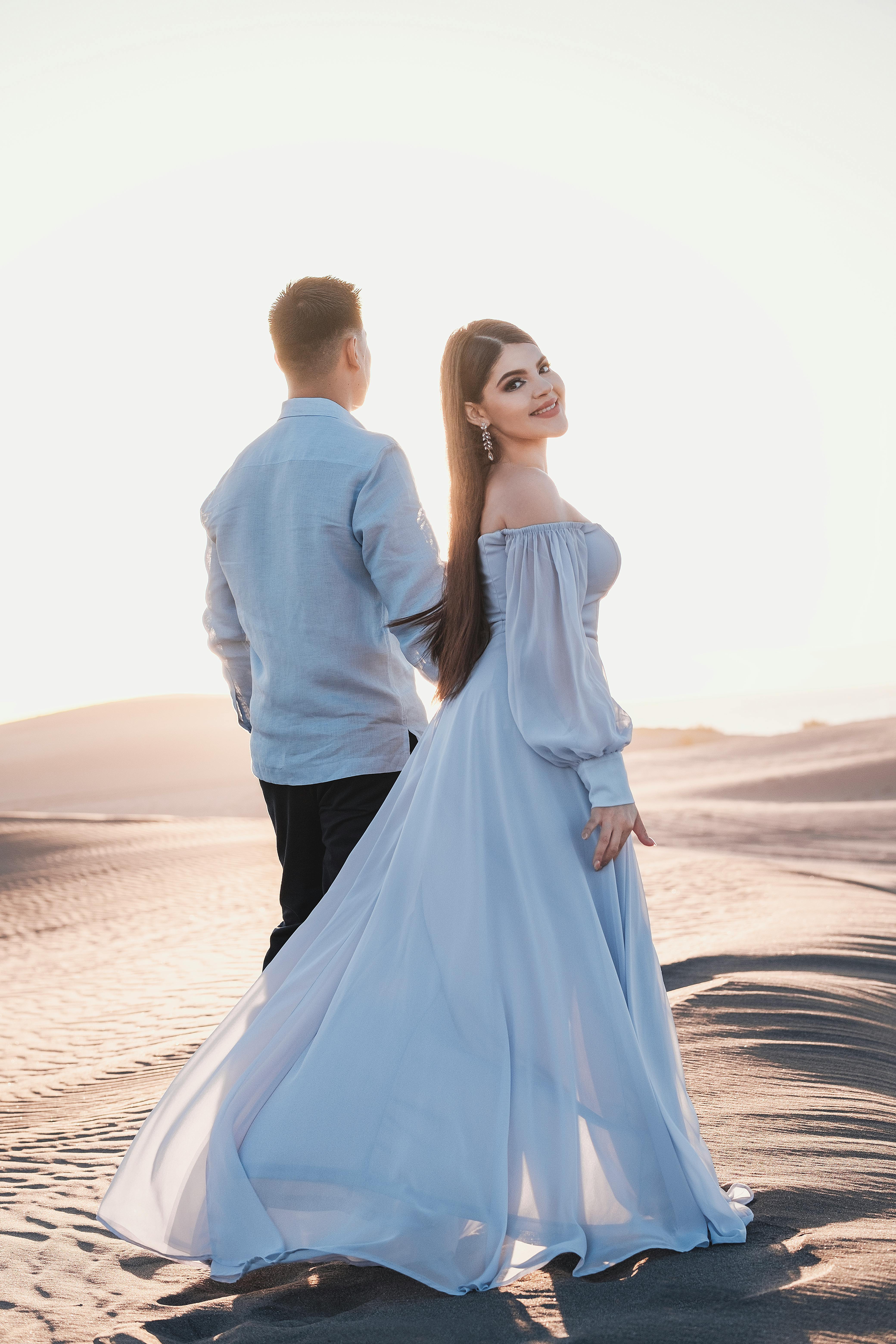A couple in elegant attire posing romantically in a sunlit desert landscape.