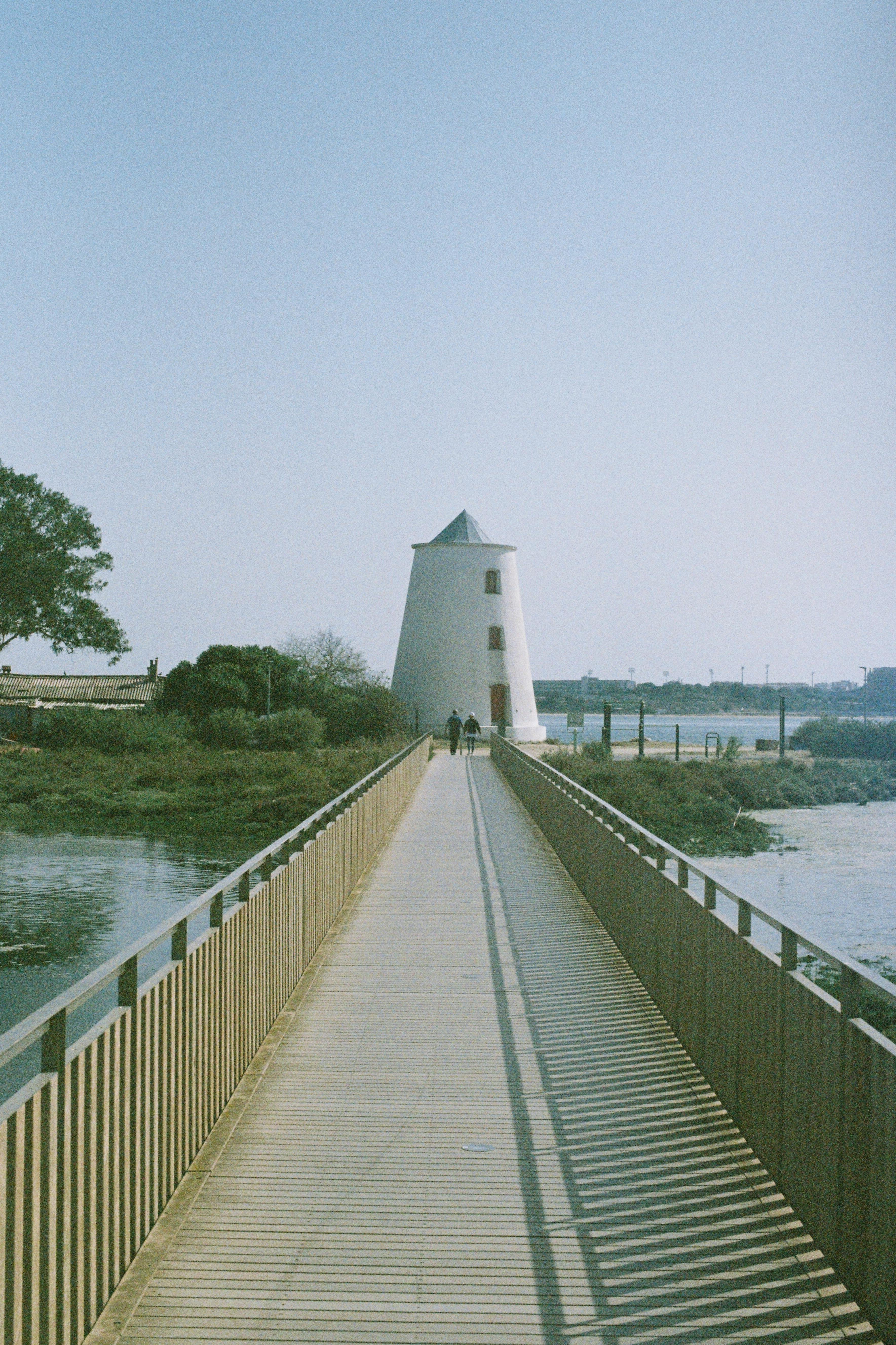 A scenic vertical shot of a lighthouse at the end of a footbridge in Lisbon, Portugal.