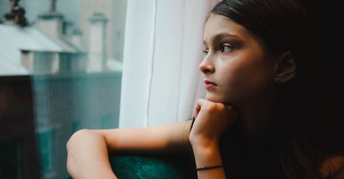 A contemplative young girl with black hair gazes thoughtfully out a window in Melbourne.