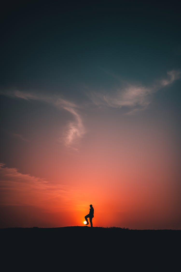 Silhouette Of Person Standing With Leg Raised At Sunset