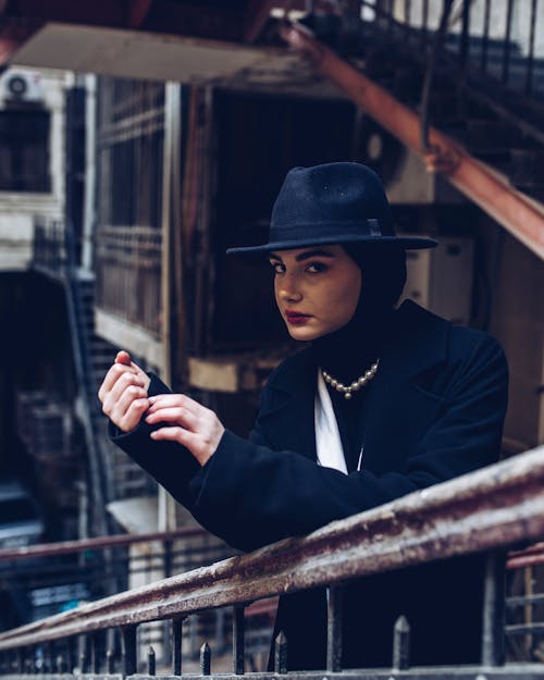 Portrait of a Young Woman Wearing a Fedora Leaning on a Staircase Handrail