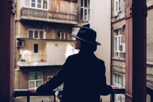 Free A woman in a black coat and hat stands on a balcony, overlooking urban buildings. Stock Photo