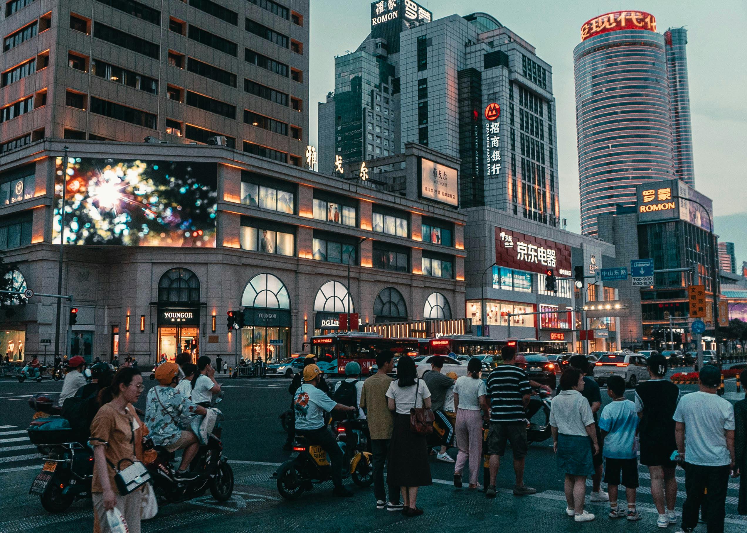 Pedestrians and vehicles at a bustling city street with skyscrapers in the background.